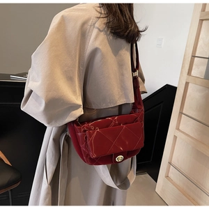 Detail of dark red quilted patent leather saddle bag worn over a khaki trench coat