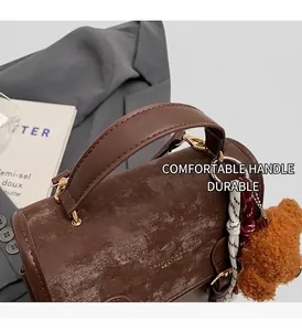 Dettaglio di una borsa vintage marrone con ciondolo a orsetto e finiture dorate
