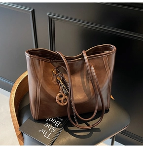 Close-up of matte dark brown PU leather tote bag with decorative pendant on black chair