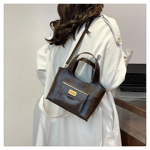 Détail du sac en cuir marron foncé poli avec plaque dorée sur un trench-coat minimaliste