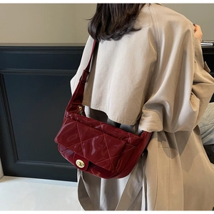 Detailed view of burgundy quilted leather saddle bag worn with a beige autumn coat