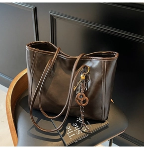 Detail of dark brown faux leather tote bag with gold key and knot charm on a vintage chair