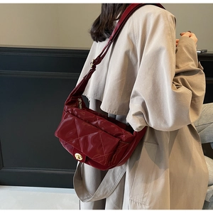Detail of burgundy quilted leather saddle bag with gold clasp shown on a model