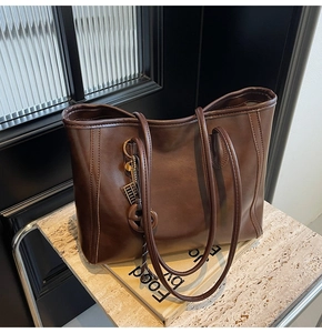 Detail of a brown leather tote bag on marble stand with stylish shoulder straps and metal charms
