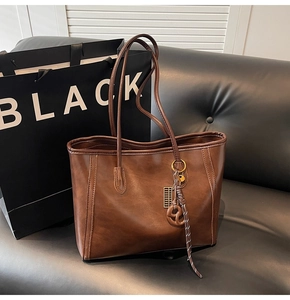 Detail of dark brown leather tote bag with gold metal hardware and woven tassel charm