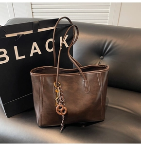 Close-up of deep brown leather tote bag featuring a decorative knotted charm and long straps