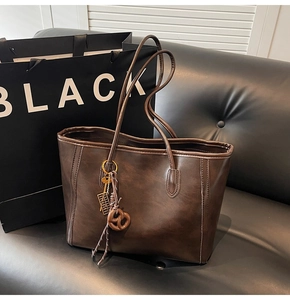 Detail of dark brown leather tote featuring vintage charms on a black sofa background
