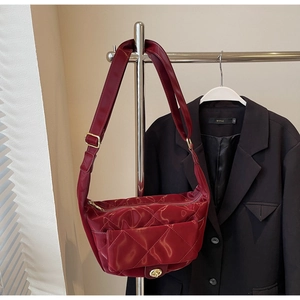 Detail of dark red quilted saddle bag with golden twist lock and wide shoulder strap