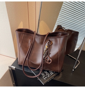 Detail of dark brown tote bag with smooth leather finish and decorative pretzel charm