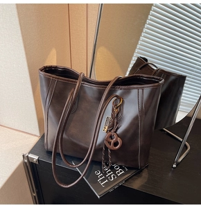Detail of a dark brown vintage faux leather tote bag with a pretzel charm on a wooden shelf
