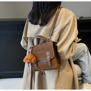 Dettaglio di uno zaino vintage in pelle marrone con fibbie in metallo e un ciondolo a cane morbido