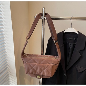 Detailed close-up of brown quilted shoulder bag with metal turn-lock and wide strap