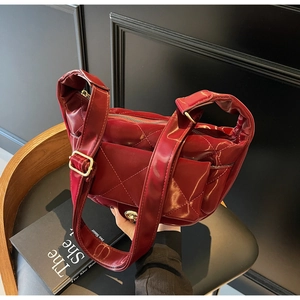 Macro shot of wine red quilted patent leather shoulder bag with gold metal buckle and wide strap