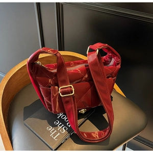 Quilted dark red patent leather saddle bag with gold hardware on a vintage wooden chair