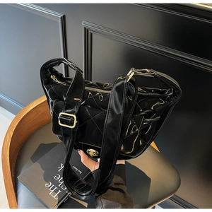 Close-up of black patent leather saddle bag with diamond quilting and gold lock