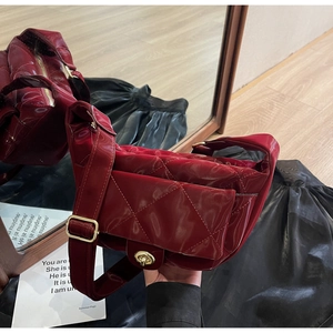 Detail of dark red quilted saddle bag featuring a gold turn-lock and glossy finish