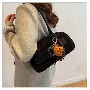 Détail du sac d'épaule en daim noir avec boucle en métal et breloque ours en peluche