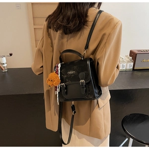 Dettaglio di uno zaino vintage in pelle nera con fibbie e ciondolo a forma di orsetto