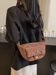 Quilted glossy brown crossbody saddle bag with golden clasp shown on shoulder