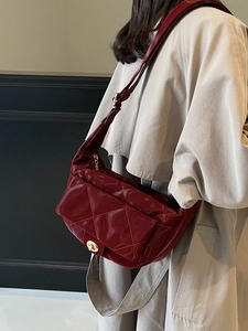 Burgundy quilted crossbody saddle bag with gold metal buckle on a beige trench coat