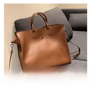 Detail view of large brown tote bag with metal buckle on a gray sofa for office use
