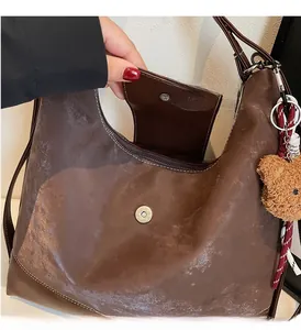 Detail of brown vintage tote bag showing white stitching, magnetic buckle and bear charm