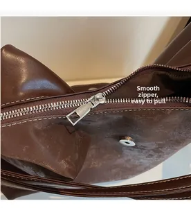 Detail view of smooth metal zipper and magnetic buckle on dark brown leather tote