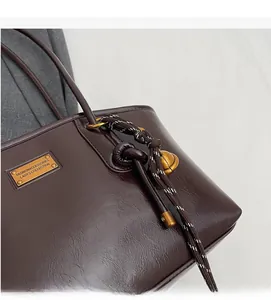 Close-up of dark brown wax leather tote with gold metal tag and decorative knotted rope charm