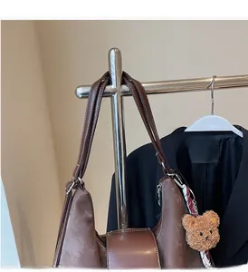 Detail of a brown leather tote with suede panels and a plush bear charm on a metal stand