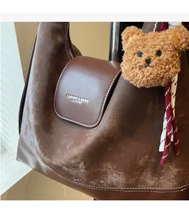 Macro detail of dark brown leather tote with white contrast stitching and bear charm