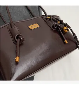 Close-up of deep brown retro leather tote bag with gold logo plaque and bell charm