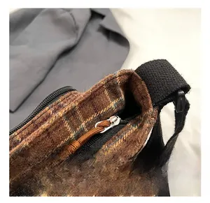 Detail showing silver metal zipper and woven puller on brown checkered canvas shoulder bag