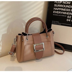 Detail of tan bucket bag showing horizontal texture and large silver metal buckle strap