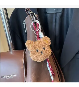 Brown teddy bear bag charm with metal clip and woven strap on a leather handbag