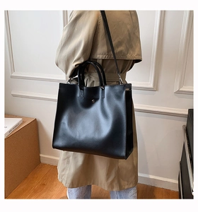 Detail of a large black tote bag featuring glossy leather and a silver metal snap button