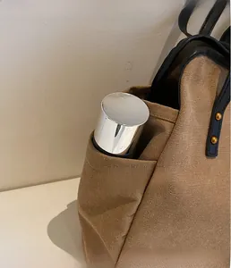 Detail of canvas tote bag side pocket with a metallic bottle and leather trim with gold studs