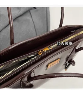 Close-up of smooth gold zipper and metallic brand plate on dark brown leather tote bag
