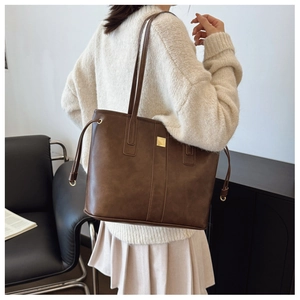 Detail of dark brown tote bag with gold metal logo and stitching on matte leather