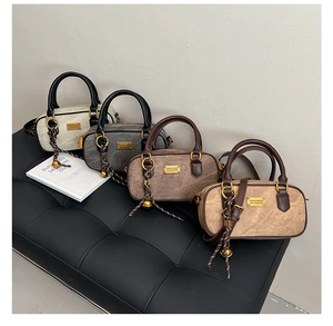 Four retro Boston bags in matte neutral tones on a dark leather bench with soft lighting