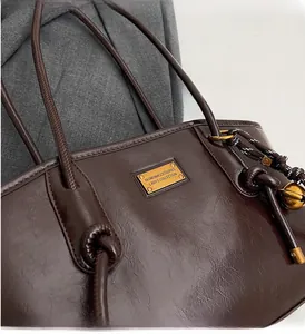 Detailed shot of dark brown glossy leather tote with golden logo plate and knot charm