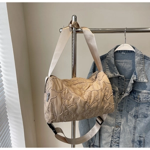 Detail of floral quilted texture on beige canvas cylinder shoulder bag with wide strap