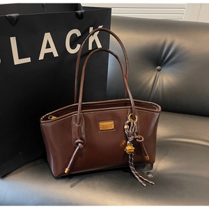 Detail of dark brown glossy leather tote bag with gold metal plaque and woven tassel