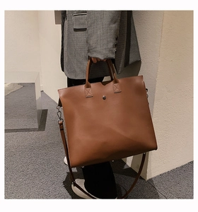 Brown leather tote bag shown in use with adjustable shoulder strap and metal detail