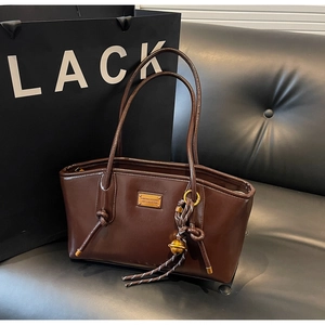Detail of a shiny dark brown vintage tote bag with a golden logo plate and knot handle