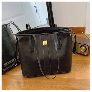 Detail showing high-gloss black tote bag with gold square plaque and drawstring side