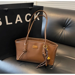 Detail of a brown leather tote bag with metal plaque and decorative knotted handle