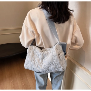 Detailed close-up of light blue quilted crossbody bag featuring floral stitching and wide strap