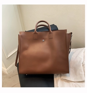 Detail view of large brown tote bag showing matte leather texture and metal snap closure