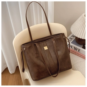 Detail of dark brown faux leather tote bag with gold metal buckle and drawstring decor