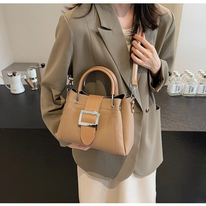 Detail of khaki bucket bag with silver metal buckle and textured finish on a blazer